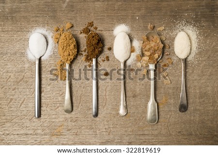 Six teaspoons of assorted sugar spilling onto a wooden background Royalty-Free Stock Photo #322819619