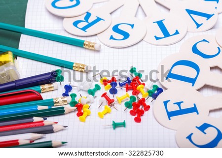Set of colorful wooden pencils yellow green red pink orange blue and brown lying in row on table with white paper sheet with pins and alphabet, horizontal picture