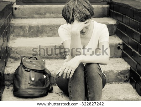 A woman sits on the concrete stairs in a very depressed mood, lying next to her on the stairs of her backpack.
