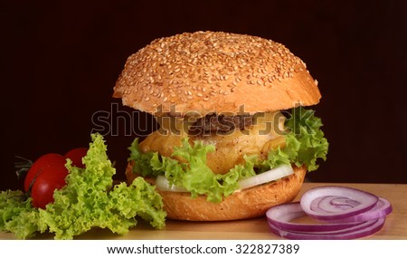 One big tasty appetizing fresh burger of green lettuce cheese bacon slice meat cutlet and white bread bun with sesame seeds and potato chips on wooden table closeup, horizontal picture
