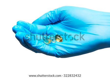 Close up of soft gel capsules with golden color oil supplements on female doctor's hand in blue sterilized surgical glove against white background