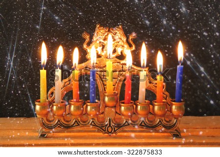Image of jewish holiday Hanukkah background with menorah (traditional candelabra) Burning candles over black background with glitter overlay