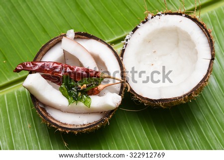 Coconut with Kashmiri chilli/chilly, curry leaves on a banana leaf top view .Used in cooking, frying,seasoning for sambar, chutney. coconut oil is used in soaps, cosmetics. red chilly Kerala India . 