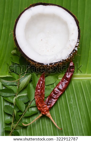 Coconut with Kashmiri chilli/chilly, curry leaves on a banana leaf top view .Used in cooking, frying, seasoning sambar, chutney. coconut oil is used in soaps, cosmetics. dry red chilly Kerala India.