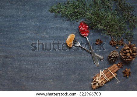 Christmas dark background with old spoon and fork, mandarin, cinnamon, anise tree and pomegranate