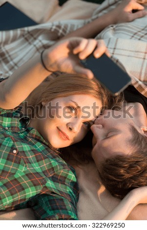 Young couple lying in the grass. They take self picture.