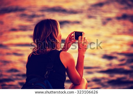 woman holding her cell phone along a river taking pictures with a shallow depth of field and a retro toned instagram filter