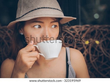 Asian woman drinking a cup of coffee. Vintage retro style photo with color filters, vignette effect, and some fine film noise added.