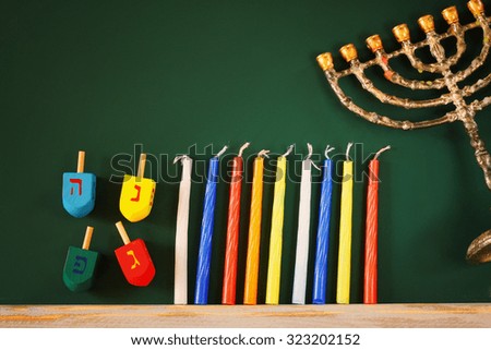 low key image of jewish holiday Hanukkah with menorah (traditional Candelabra) and wooden dreidels spinning top over chalkboard background, room for text 