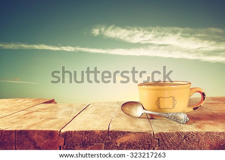 front image of coffee cup over wooden table in front of sky sunset 