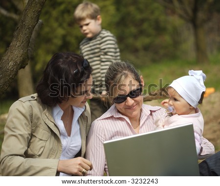 Young mothers are sitting on the ground in the garden and using a laptop.