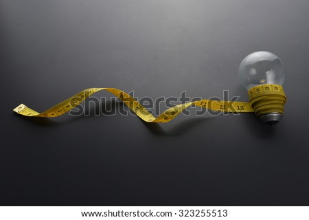 Lowlight key of light bulb and Yellow measuring tape with water drop on grey background