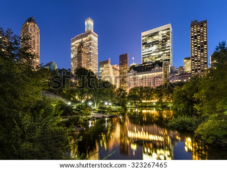 Manhattan skyscrapers illuminated in early evening light.The buildings of Central Park South are reflected in the Central Park Pond. New York City