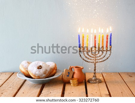 image of jewish holiday Hanukkah with menorah (traditional Candelabra), donuts and wooden dreidels (spinning top). glitter overlay 