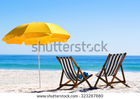 Pair of sun loungers and a beach umbrella on a deserted beach; perfect vacation concept  Royalty-Free Stock Photo #323287880