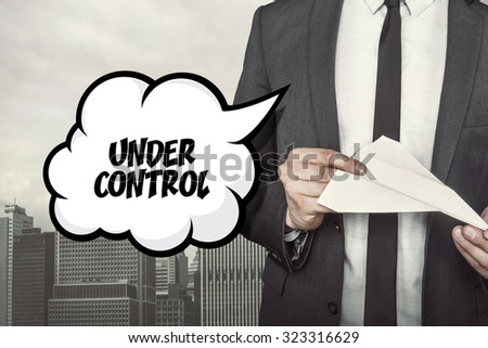 Under control text on speech bubble with businessman holding paper plane in hand on city background