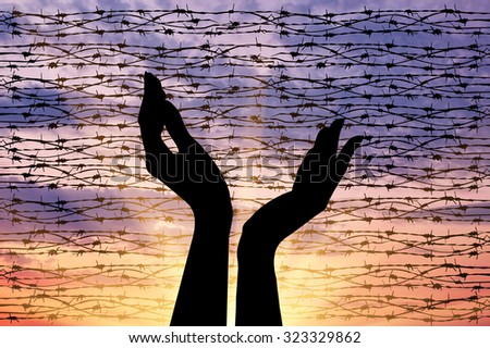 Concept of the religion of refugees. Silhouette outstretched arms to the sky against a background of barbed wire at sunset