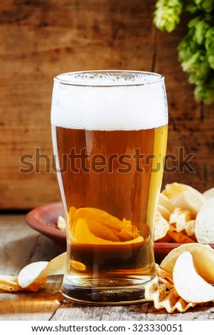 large glass of light beer and potato chips on a wooden background, selective focus