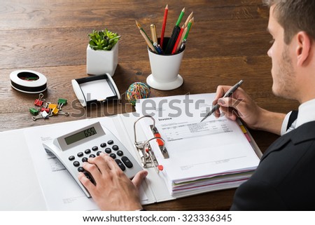 Close-up Of Businessman Calculating Receipt With Calculator At Desk