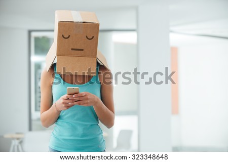 Young teen girl with a box on her head texting with her mobile phone, adolescence and social isolation concept