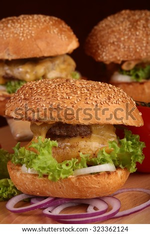 Big tasty appetizing fresh burgers of green lettuce red tomato cheese and bacon slice meat cutlet and white bread bun with sesame seeds closeup, vertical picture