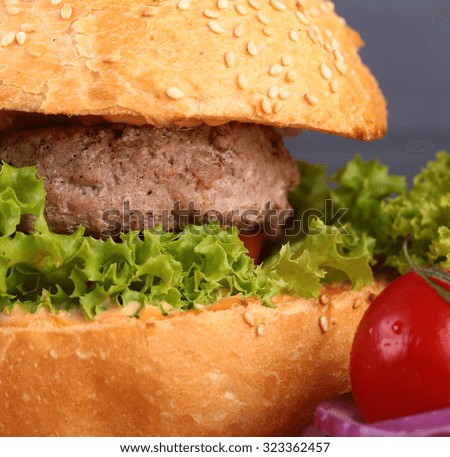 Big tasty appetizing fresh burger of green lettuce cheese bacon slice meat cutlet and white bread bun with sesame seeds and potato chips on wooden table closeup, square picture