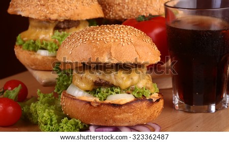 One big tasty appetizing fresh burger of green lettuce cheese bacon slice meat cutlet and white bread bun with sesame seeds and potato chips on wooden table and cola, horizontal picture