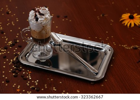Aromatic irish coffee black and brown colors with whipped cream poured syrup in clear glass and spoon on metal tray on table with coffee beans stars and yellow flower, horizontal photo
