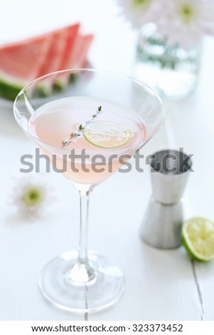Cocktail mocktail drink in a martini glass decorated with a slice of lime and garnish with a slice of watermelon and flowers in the background