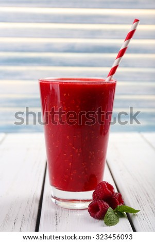 Raspberry cocktail and raspberries on wooden surface on light background