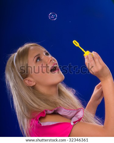 young beautiful blond inflate soap bubbles on a blue background