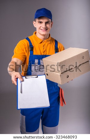 Delivery. Portrait of a young man in work clothes with boxes on a gray background