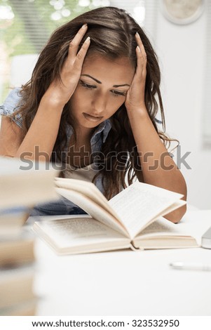 Portrait of tired beautiful teenage girl holding her head and learning.