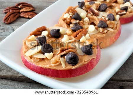 Autumn apple rounds with peanut butter, chocolate chips and nuts, on white serving plate Royalty-Free Stock Photo #323548961