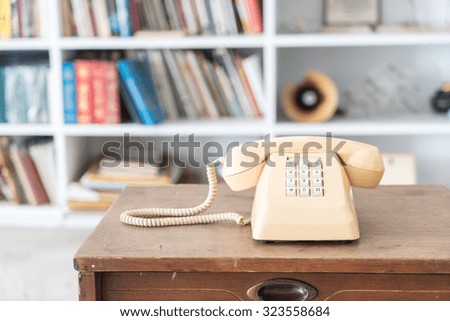 Cream vintage phone on wooden table, on bookshelf background