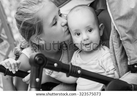Happy little sister kissing baby brother in a stroller  ( black and white )