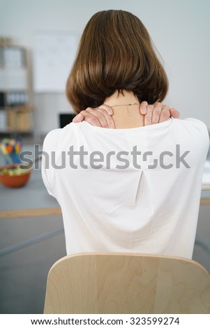 Rear View of a Tired Office Woman Sitting at her Desk, Massaging the Back of her Neck with her Two Hands.