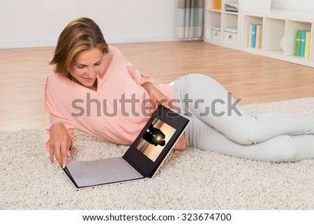 Young Woman Smiling While Looking At Photo Album In Living Room