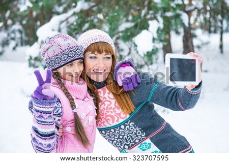 Mom and daughter have fun in the winter. Two girls take a selfie. Mom and daughter are photographed in winter forest, family values. Two girls make a photo on the flatbed in snowy park