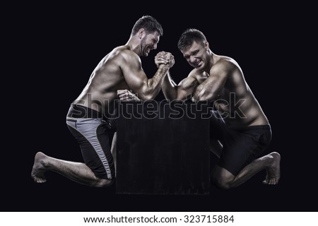 Two young athletes have a hard arm wrestling match on a black box shirtless