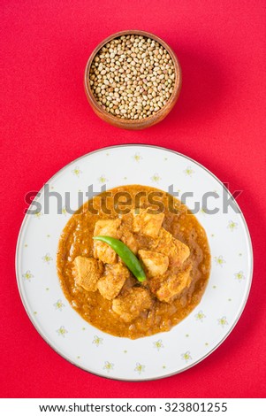 Indian chicken curry - Overhead view of spicy Indian chicken curry served on a plate pictured next to a bowl of coriander seeds, a key ingredient. Natural light used.