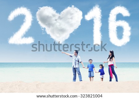 Portrait of happy family walking on the beach and looking at cloud shaped numbers 2016