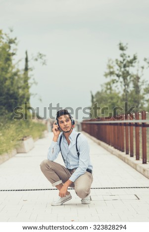Young handsome man with short hair and beard wearing suspenders and listening to music in an urban context