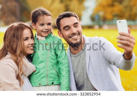 family, childhood, season, technology and people concept - happy family taking selfie by smartphone in autumn park