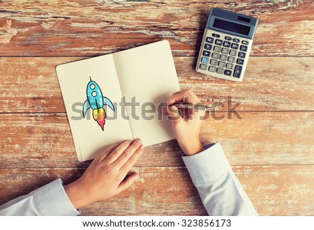 business, education, people and technology concept - close up of female hands with calculator and pen drawing rocket in notebook on table