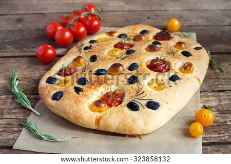 Homemade focaccia with red and yellow cherry tomatoes, black olives and rosemary on a wooden table