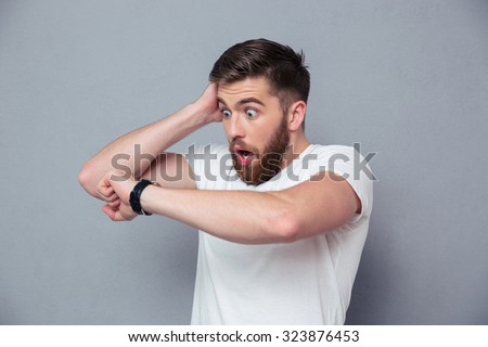 Portrait of a shocked man looking on wrist watch over gray background Royalty-Free Stock Photo #323876453