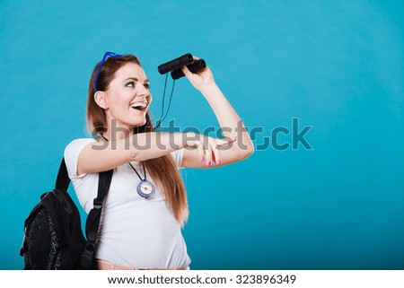 Summer holidays and tourism concept. Lovely tourist woman with backpack compass looking through binoculars on blue