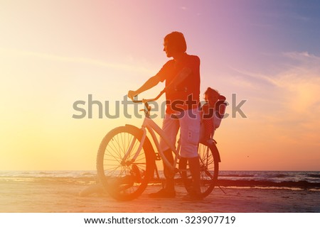 Silhouette of father and baby biking at sunset beach