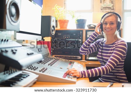 Portrait of young radio host wearing headphones using sound mixer in studio